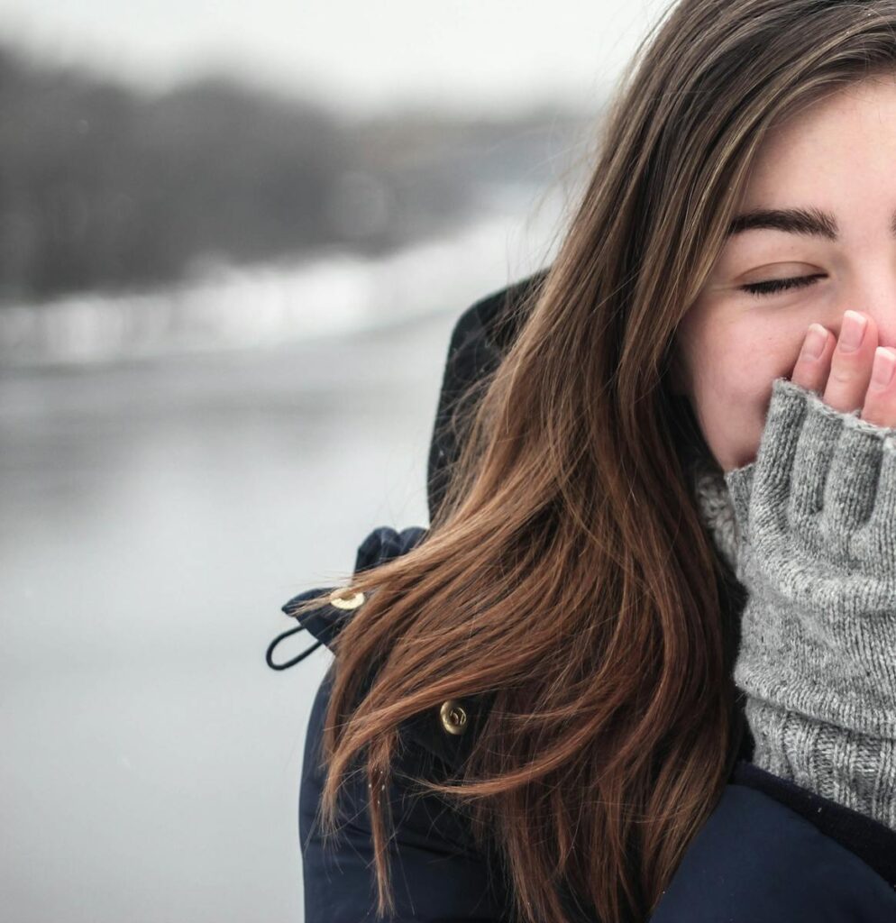 A woman enjoys the cold weather with a joyful smile, dressed warmly in winter clothing.