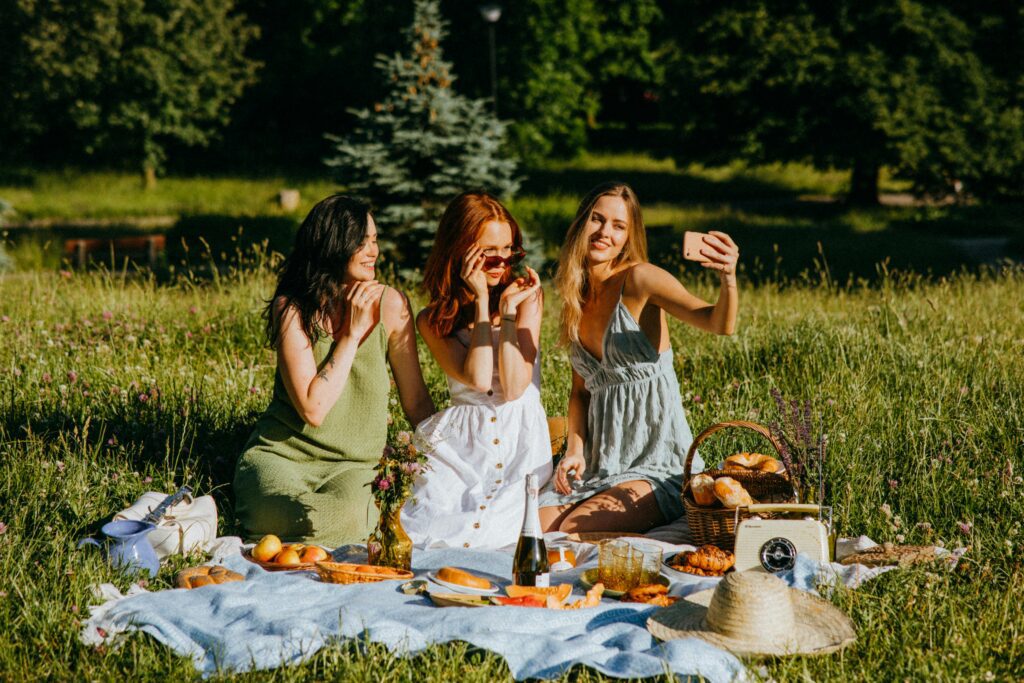Three women enjoying a summer picnic in a park, capturing a selfie together.