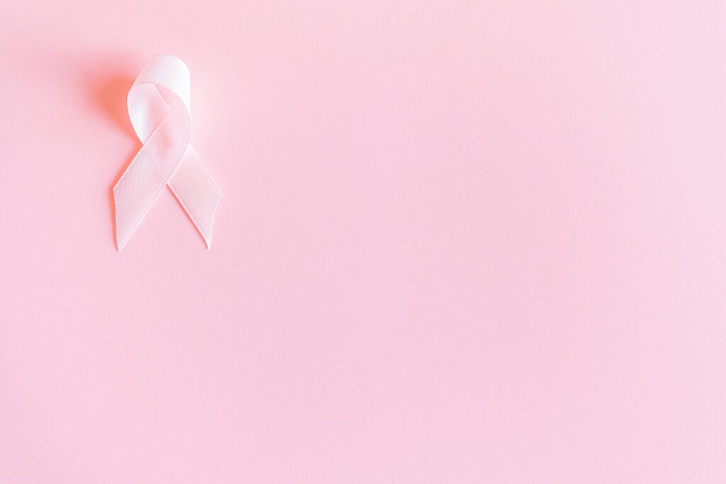 A pink ribbon on a soft pink background symbolizing breast cancer awareness and solidarity.