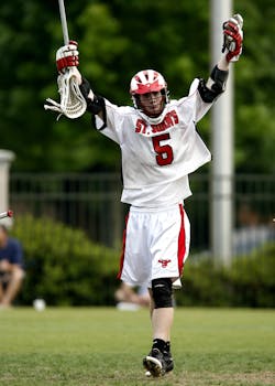 Lacrosse player celebrating a victory with arms raised, outdoor sports action.
