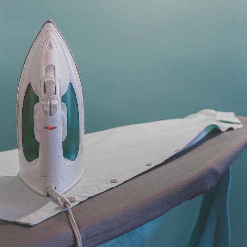 white and teal steam clothes iron plugged on ironing board